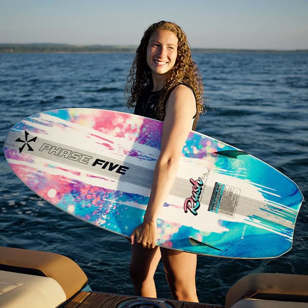 Girl holding a vibrant surfboard on a sunny day by the water, ready for surfing.