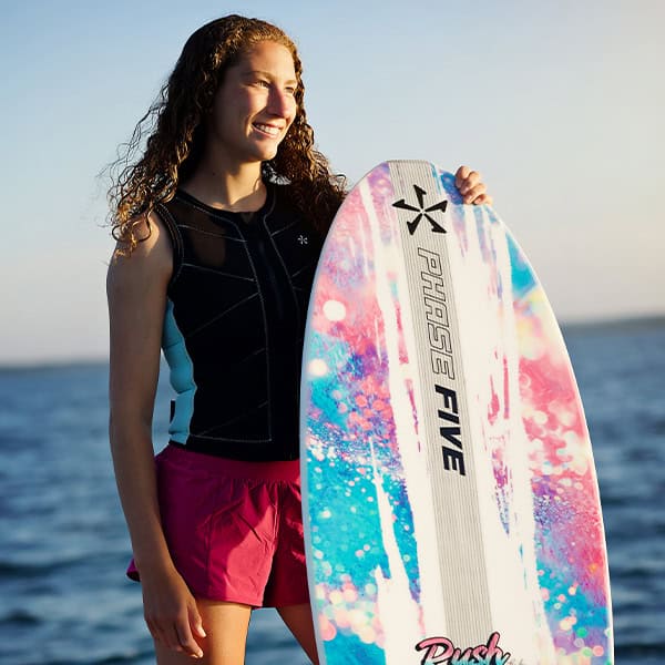 Young woman smiling with a paddleboard by the ocean during sunset, enjoying water sports and outdoor activities.