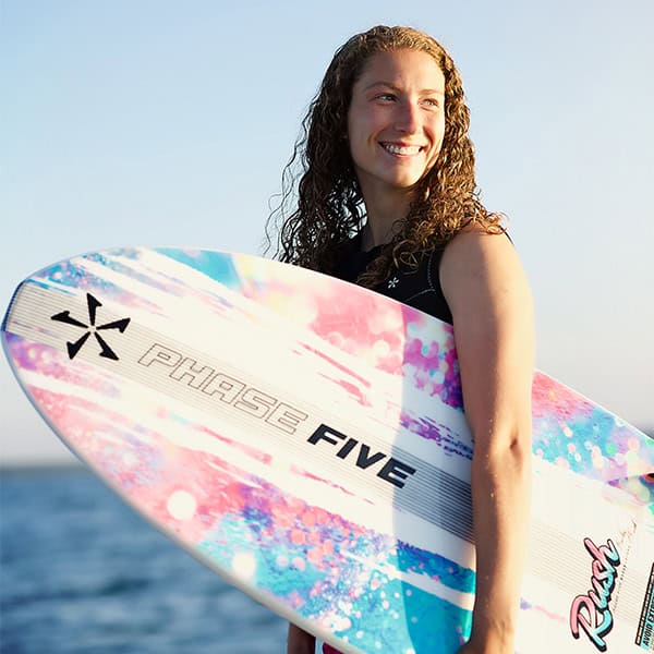 Young woman smiling with a vibrant surfboard at the seaside.